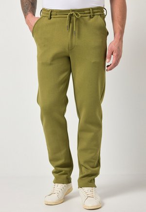 Uomo con pantaloni jogger verde oliva con vita con coulisse e scarpe da ginnastica bianche, in piedi con le mani rilassate ai lati.