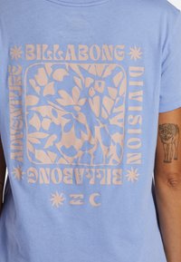 Camisa de tirantes de color azul claro que presenta un gran gráfico floral rosa y el texto "BILLABONG ADVENTURE" y "DIVISION" en la parte posterior.