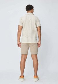 Chemise à manches courtes de couleur beige clair avec des rayures verticales orange et jaunes. Associée à un short beige et des baskets blanches avec des accents orange.
