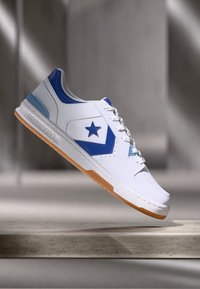 Hvit sneakers med blå detaljer, med en stjernelogo, gummiert såle og teksturerte paneler. Snørebånd og polstret krage inkludert.