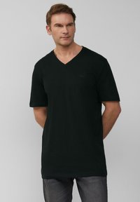 Czarny t-shirt z dekoltem w serek wykonany z miękkiej bawełny. Krótkie rękawy, luźny krój, minimalne logo na klatce piersiowej. Noszony z ciemnymi jeansami.