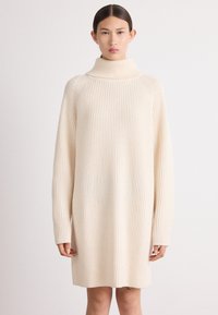 Krémové oversized rebrované pletené šaty s vysokým golierom a dlhými rukávmi, s uvoľnenou siluetou.