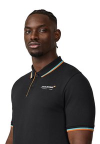Czarna koszulka polo z bawełny, z krótkim kołnierzykiem w pomarańczowe i niebieskie akcenty oraz logo McLaren na lewej piersi.