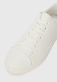 Hvit lærsneaker med rund tå, teksturert såle og flate snorer. Glatt overflate og minimalistisk design uten ekstra mønstre.