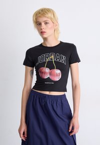 Black cropped t-shirt featuring "JORDAN" text, cherry graphics, and "Established 1984." Paired with navy drawstring pants.