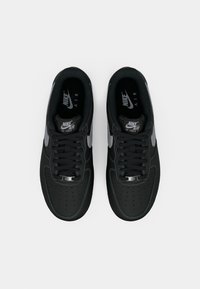 Black Nike Air Force 1 sneakers feature a smooth leather upper, perforated toe box, dark laces, and gray accents, with a cushioned sole.