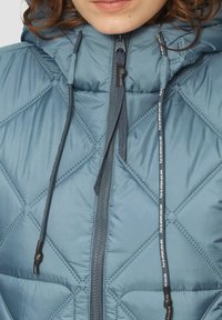 Gestepptes blauer Pufferjacke mit Kapuze, Frontreißverschluss und Kordeln. Das Material hat eine glatte Textur mit dunklen Akzenten.