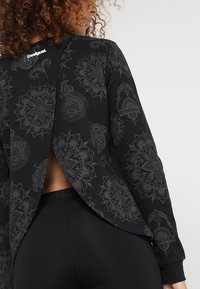 Felpa nera a maniche lunghe con complessi motivi paisley grigi, caratterizzata da un design con schiena aperta e un logo sul colletto.