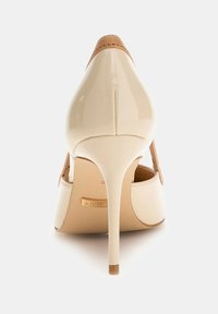 Beżowe lakierowane szpilki z wąskim noskiem, brązowymi akcentami i smukłym obcasem w stylu stiletto. Wnętrze z logotypem i gładkim wykończeniem.