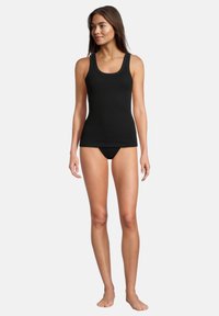 Top senza maniche nero a coste con scollatura a giro, design aderente e taglio classico, abbinato a lingerie nera coordinata, indossato da una modella.