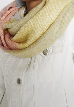 Écharpe en laine douce multicolore jaune pastel, rose et gris, enroulée autour du cou sur une veste en denim blanc avec boutons métalliques.