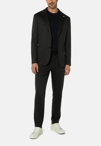 Dunkelgrauer Anzug mit einem taillierten Blazer mit Revers und passenden Hosen. Kombiniert mit einem blauen Hemd und weißen Sneakers für den Kontrast.
