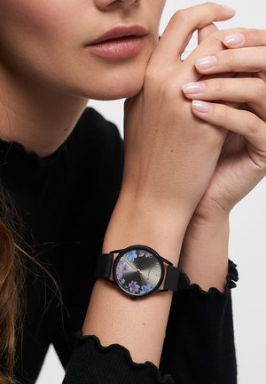 Schwarze Armbanduhr mit einem runden Ziffernblatt, das ein florales Muster in Lila und Blau auf einem dunklen Hintergrund zeigt. Glatter Silikonarmband, minimale Akzente.