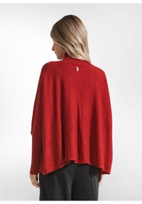 Rode gebreide pullover trui met een hoge hals, voorzien van geribbelde manchetten en een losse, vloeiende pasvorm die aan de achterkant taps toeloopt.