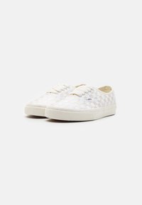 Niedrig geschnittene Schnürsneaker mit beigem und weißem Schachbrettmuster sowie Gummisohle, seitliche Ansicht auf einem weißen Hintergrund.