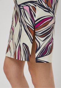 Jupe à motif floral présentant diverses nuances de rose, marron et bleu marine sur un fond crème, avec une fente latérale pour un détail de design supplémentaire.