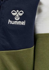 Pánská mikina na zip s námořnickými modrými a olivovými panely, měkkou texturou a bílým vyšívaným logem na hrudi.