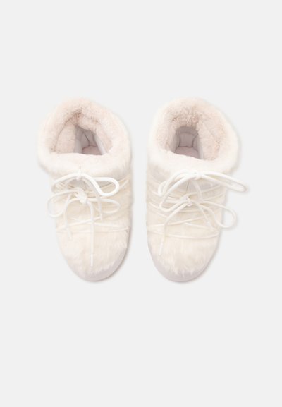 Paire de chaussons d'hiver blancs et poilus avec une doublure douce et des lacets, vus de dessus sur un fond clair.