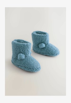 Blaue, flauschige Hausschuhe aus weichem, strukturiertem Material. Knöchelhöhe mit abgerundeter Spitze, ausgestattet mit jeweils zwei Pompon-Akzenten an jeder Seite.