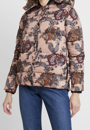 Pink puffer jacket with detailed black, brown, and red animal and foliage print worn with blue jeans, hands relaxed by sides.