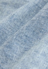 Hellblauer Stoff mit strukturiertem Gewebe, der ein weiches, leicht ausgebleichtes Aussehen und subtile Farbvariationen aufweist.