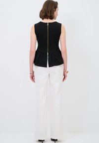 Schwarzes Peplum-Top mit einem Reißverschluss auf der Rückseite, kombiniert mit weißen weit geschnittenen Hosen, die eine glatte Textur und klare Linien aufweisen.