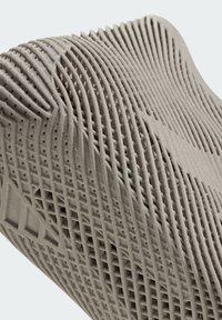 Gros plan sur un objet imprimé en 3D avec une texture et des couches, présentant des crêtes courbes et répétitives ainsi qu'un motif en grille en matériau gris.