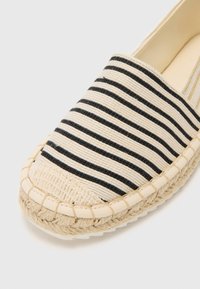 Raittipintainen espadrilles-kengät beige ja mustana, joissa on neulottu kangasü верх ja jute-köysi pohja. Pyöreä kärki ja tikatut yksityiskohdat.