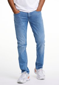 Light blue denim jeans with a straight-leg cut, featuring side pockets and subtle stitching, paired with white and gray athletic shoes.