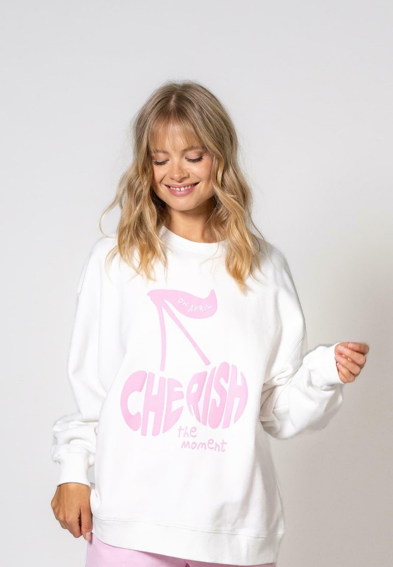 Sweatshirt blanc en coton, présentant un grand motif rose avec le texte "CHÉRISSEZ le moment" et une illustration de talon haut rose.