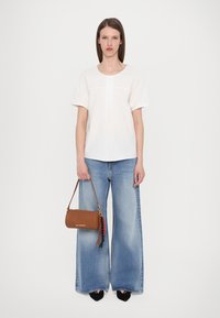 White short-sleeve blouse, wide blue denim trousers, and a brown leather handbag with colorful tassels, set against a plain background.