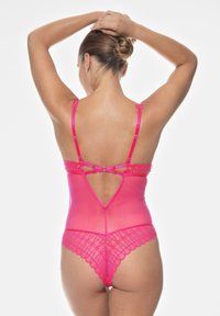 Rosa genomskinlig bodysuit med spetsdetaljer, justerbara axelremmar och en dekorativ bakspänne. Har en scalloped kant vid benöppningarna.