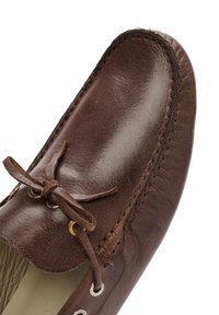 Mocasín de cuero marrón con detalles de cordones y lazo. Presenta costuras visibles y ojales metálicos, destacando un diseño clásico.
