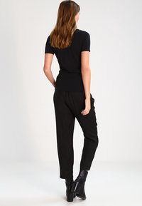 Camiseta negra ajustada combinada con pantalones negros sueltos. La modelo lleva botas de tacón negras. Tejido suave con mínima textura, diseño sencillo.