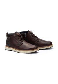 Brown leather ankle boots with a cream rubber sole, featuring lace-up front, zip closure, and textured accents on the sides.