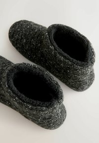 Zwarte en grijze pluche pantoffels met een geweven, textuurbeweging aan de buitenkant en een zachte voering. Pantoffelstijl met een afgeronde neus en een lage hak.