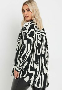 Black and white patterned blouse with abstract stripes, long sleeves, and a relaxed fit. Fabric has a smooth texture with a slight sheen.