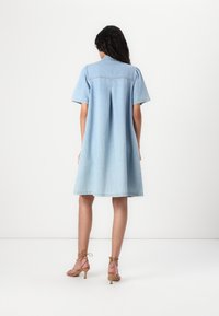 Lys blå denimkjole med korte puffede ærmer, løs pasform og en rygplissering. Kombineret med nude stropsteletter. Glat tekstur.