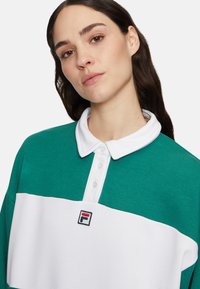 Zielona i biała koszulka polo z kołnierzykiem w szpic, zapięciem na guziki i logo Fila na piersi. Wykonana z miękkiej, teksturowanej tkaniny.
