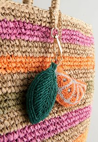 Sac en paille tissée avec des rayures roses et orange, doté d'un fermoir doré tenant des breloques en forme de feuille verte perlée et de tranche d'agrume orange.