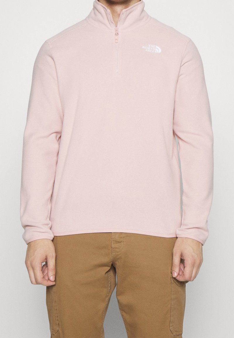 Pullover in pile rosa chiaro con collo a mezza zip, caratterizzato da un logo bianco sul lato sinistro del petto e maniche lunghe. Tessuto morbido e vestibilità casual.