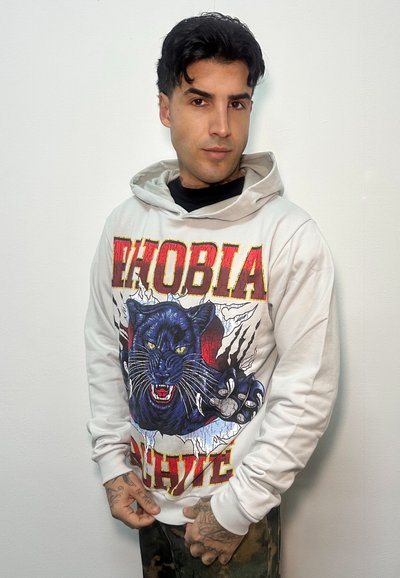 Felpa con cappuccio bianca con design grafico che presenta una pantera blu, accenti rossi e testo in grassetto. Maniche lunghe e cappuccio con coulisse.