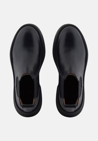 Scarpe nere in pelle senza lacci con pannelli elasticizzati sui lati, punta arrotondata e suola in gomma. L'interno presenta un accento beige vicino all'apertura.