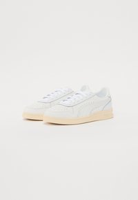 Baskets en cuir blanc avec détails perforés, bout rond et semelle plate crème. Comprend des lacets blancs et un marquage subtil.