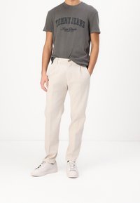 Šedé tričko s krátkým rukávem s nápisem "TOMMY JEANS New York". Krémové kalhoty na míru s plochým předním dílem a bočními kapsami. Bílé tenisky.