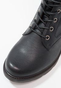 Sort læderstøvle med struktureret overflade, rund tå, snørebåndsdesign og sølvøjer. Gummisål og forstærkede sømme langs kanten.