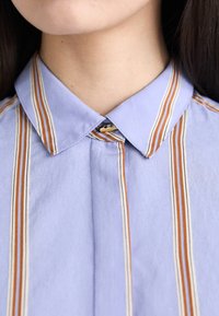 Light blue button-up shirt with vertical stripes in orange and cream. Features a classic collar and a small decorative button detail.