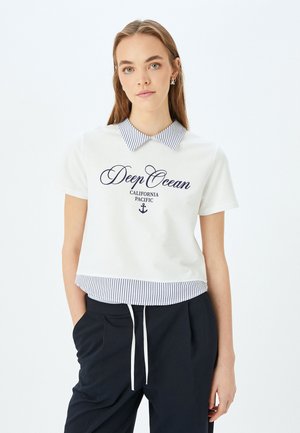 Polo bianco a maniche corte con colletto a righe blu navy, con grafica "Deep Ocean California Pacific", abbinato a pantaloni scuri.