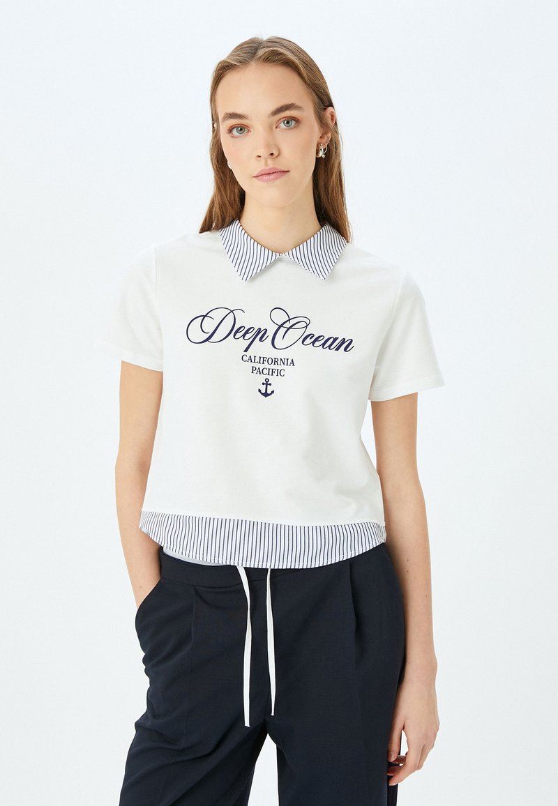 Polo bianco a maniche corte con colletto a righe blu navy, con grafica "Deep Ocean California Pacific", abbinato a pantaloni scuri.