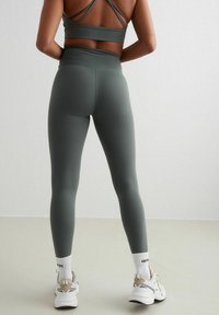 Grijze hoge taille leggings van rekbaar materiaal, gecombineerd met een bijpassend cropped top met kruisspannende bandjes op de rug.
